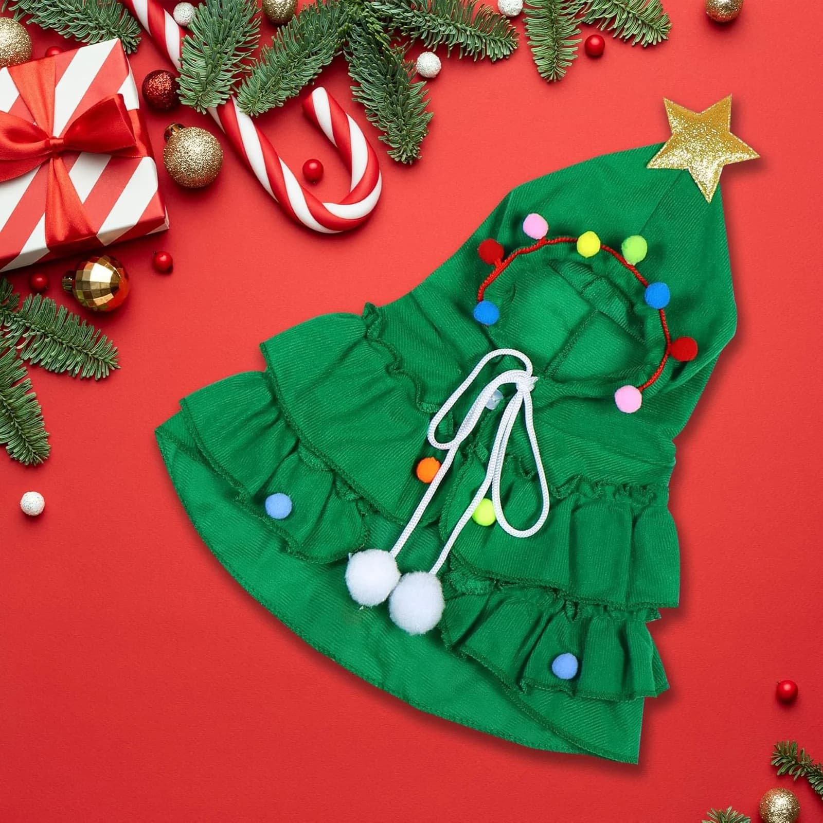 The green cape laid flat: hood with gold star, tie ribbons with pom-poms, tiered ruffles